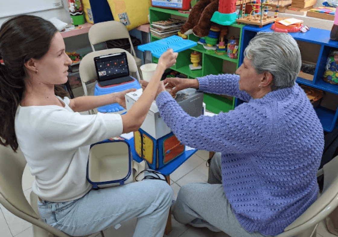 Regina and an elderly woman working on a prototype using a disposable cup and cardboard boxes