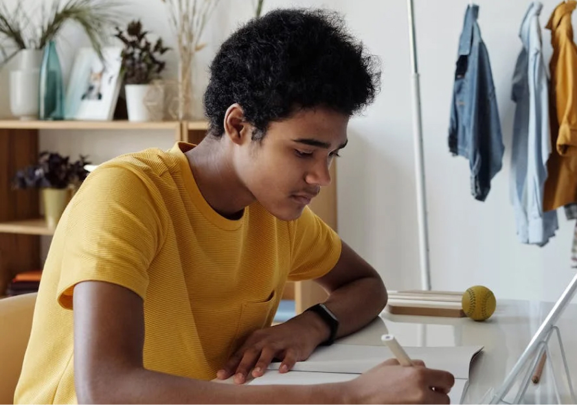 A teenager wearing a yellow t-shirt writing in a notebook