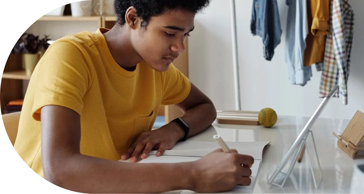 A teenager wearing a yellow t-shirt writing in a notebook